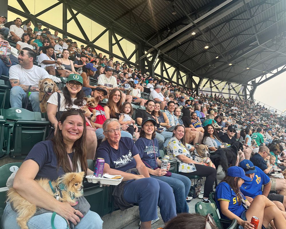 TVES team members with dogs smiling and posing during baseball game